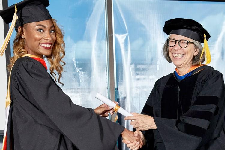 Female student in cap and gown receiving a diploma for an online masters program